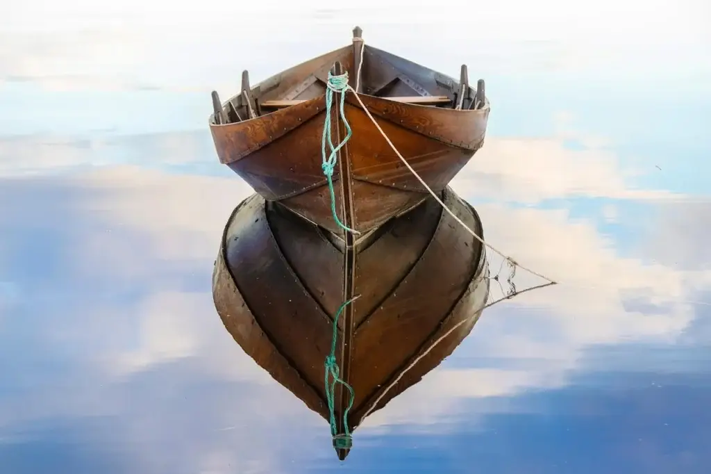 Houten roeiboot ligt aangemeerd op stil water en weerspiegelt in het wateroppervlak.