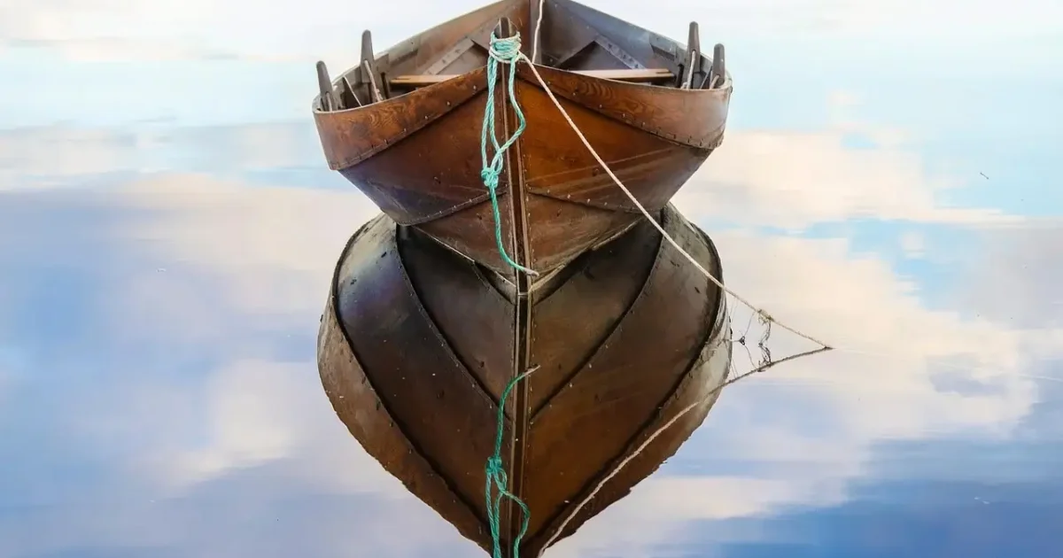 Houten roeiboot ligt aangemeerd op stil water en weerspiegelt in het wateroppervlak.